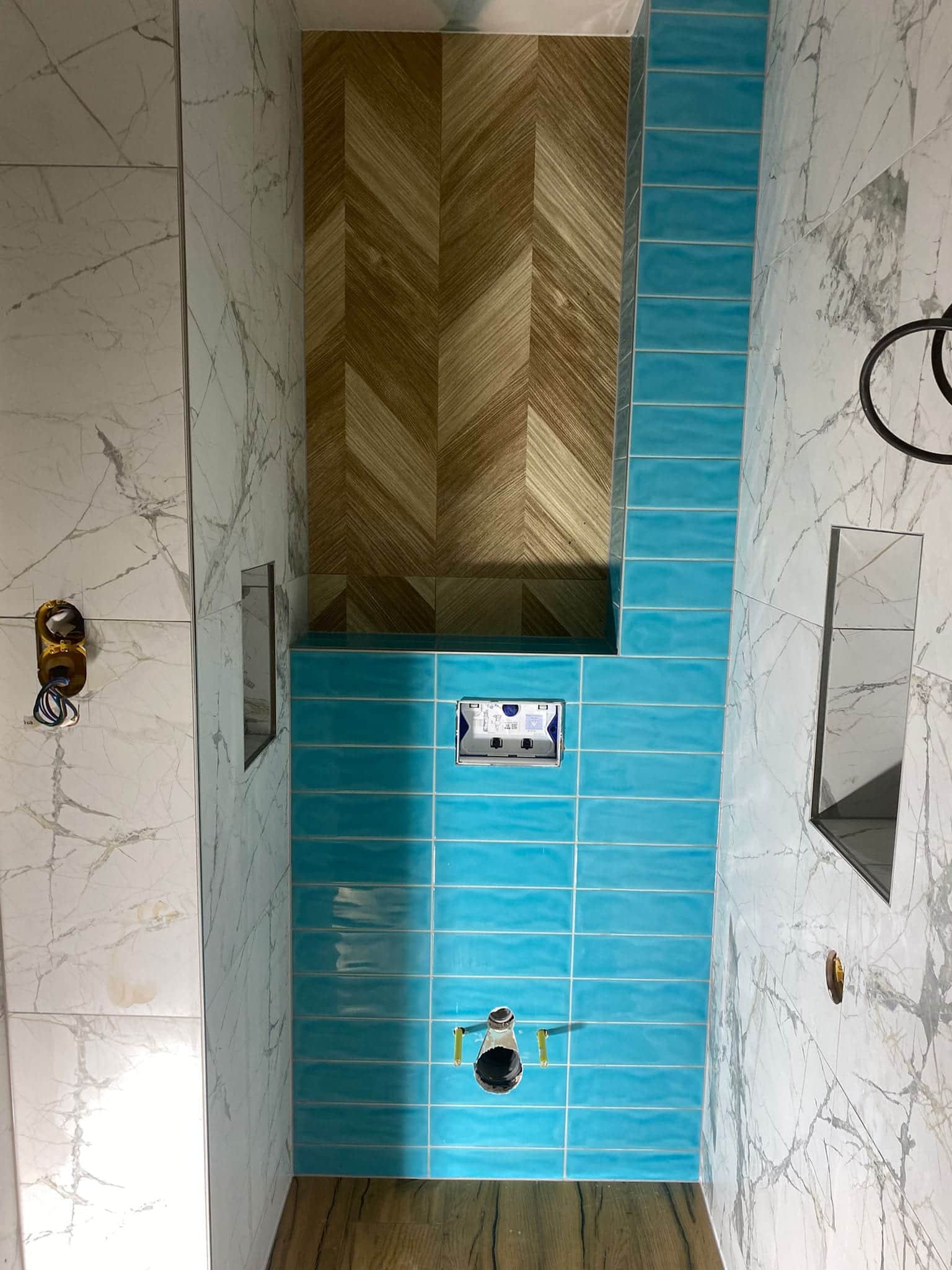 Tyrkysová predstena WC so zapusteným ovládacím tlačidlom, okolo obklad v dekore bieleho mramoru