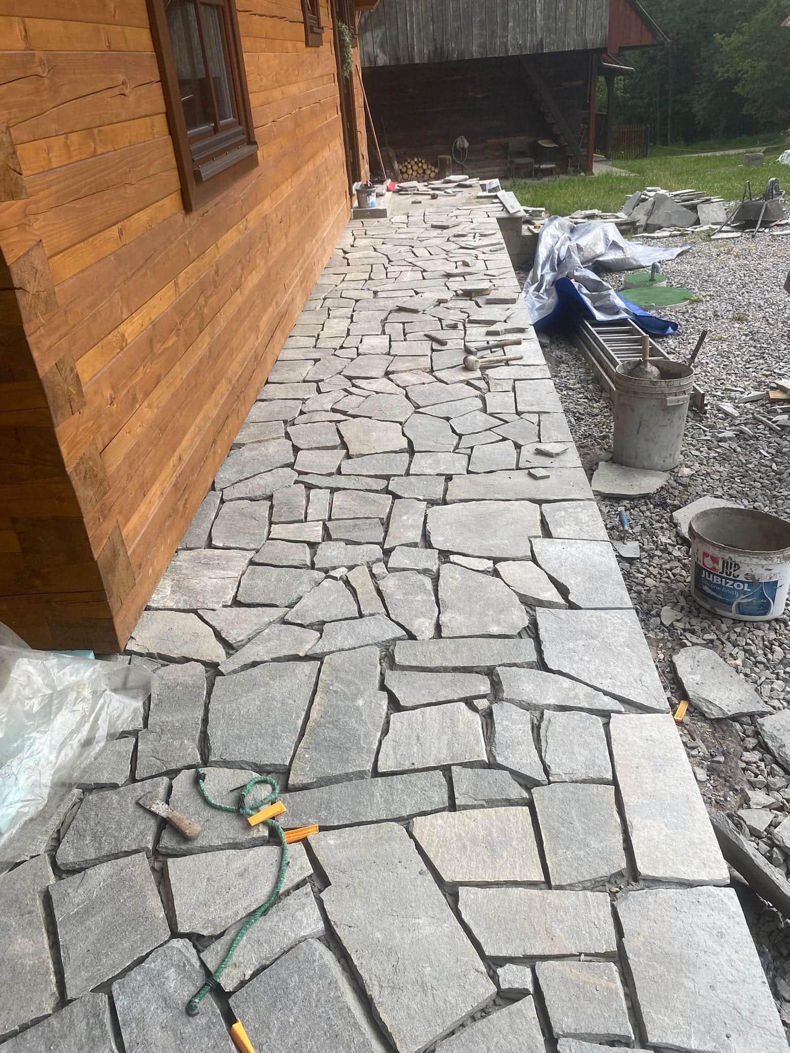 Kladenie kamenných platní pri stene chaty počas realizácie