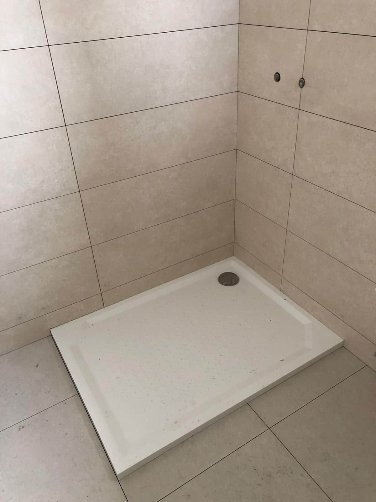 Päťuholníková sprchová vanička osadená v rohu medzi dve obložené steny