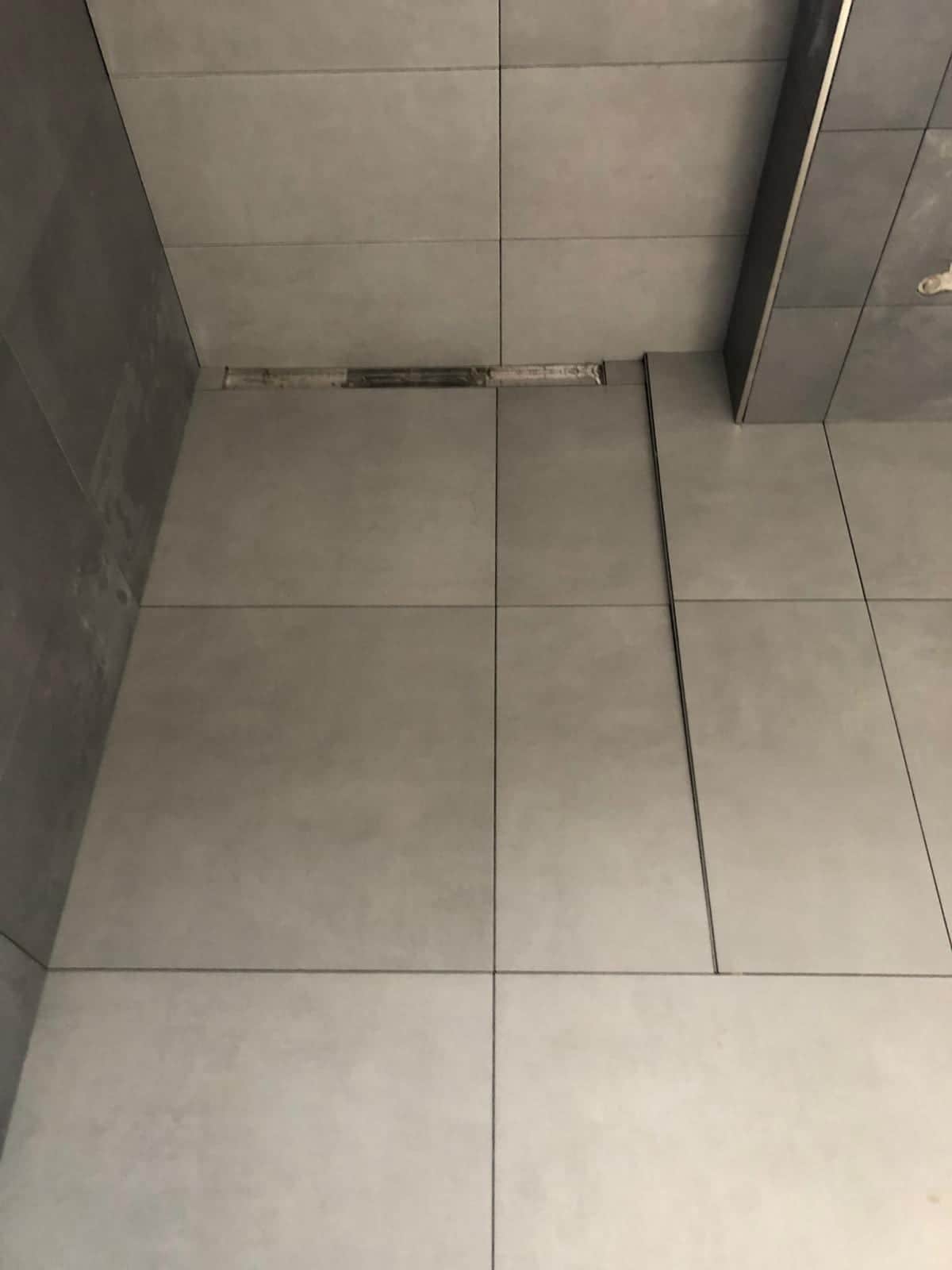 Lineárny žľab pri stene so spádom dlažby vedeným z celej plochy sprchy